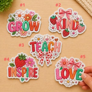 Peut inclure: Cinq écussons brodés colorés avec des motifs floraux et de fraises. Les écussons présentent les mots "GROW", "KIND", "TEACH", "INSPIRE" et "LOVE" en différentes couleurs. Chaque écusson a une bordure blanche.