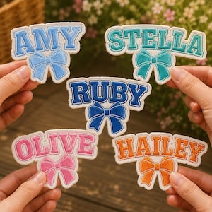 May include: Embroidered name patches in blue, teal, pink, and orange, each with a matching bow design. Names include Amy, Stella, Ruby, Olive, and Hailey. These patches are ideal for personalising clothing or accessories.
