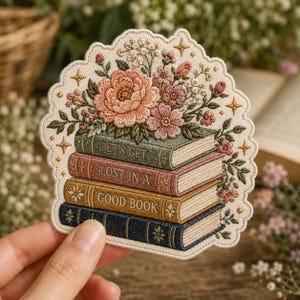 May include: Embroidered patch featuring a stack of books with floral accents. The books are labeled "LET'S GET", "LOST IN A", and "GOOD BOOK". The patch has a cream-colored border with gold star details and a bouquet of pink and peach flowers.