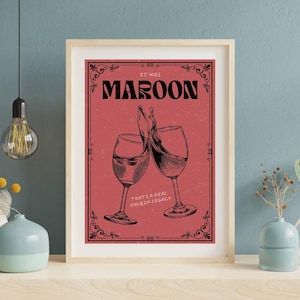 Könnte beinhalten: Gerahmter Kunstdruck mit einem weinroten Hintergrund, der zwei anstoßende Weingläser mit spritzendem Wein zeigt. Der Text lautet "IT WAS MAROON" und "THAT'S A REAL FUCKIN LEGACY". Der Druck hat einen dekorativen Rahmen.