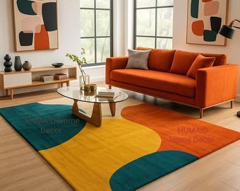 May include: A modern living room featuring a vibrant, abstract rug in teal, yellow, and orange. An orange sofa, artwork, and a glass coffee table complete the stylish decor. The rug has the text "HUMAID-Home Decor".