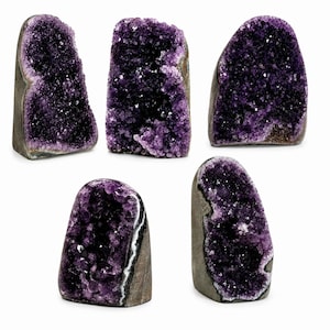 May include: Five distinct amethyst crystal geodes standing upright. Each piece features a deep purple, crystalline interior with jagged, sparkling points, contrasted by a smooth, greyish-brown natural rock exterior forming the base and sides.