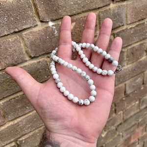 May include: White beaded necklace with a silver clasp. The beads are round and have a marbled pattern.