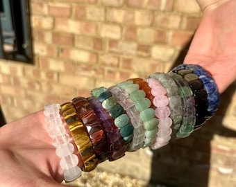 May include: A stack of colorful gemstone bracelets, including clear quartz, tiger's eye, amethyst, green aventurine, rose quartz, and blue lapis lazuli.