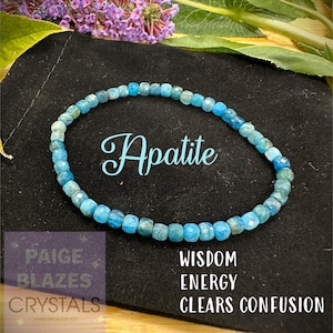 Peut inclure: Un bracelet en cristal d'apatite bleu avec le texte "Apatite" en cursive. Le bracelet est sur un fond noir avec le texte "Wisdom Energy Clears Confusion" en dessous.