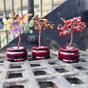 Könnte beinhalten: Drei kleine, drahtgewickelte Edelsteine ​​in Rot, Braun und Grün, jeweils auf einem dunkelroten Holzsockel.