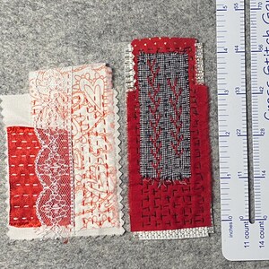 May include: Two rectangular fabric patches with detailed stitching. One has red and white lace and heart patterns, the other a black and red geometric design. A ruler with inch measurements is in the background.