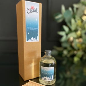 Könnte beinhalten: Ein brauner Karton mit einem weißen Etikett, auf dem "Cherish Winter Scent Reed Diffuser" steht. Die Schachtel befindet sich neben einer durchsichtigen Glasflasche mit schwarzem Verschluss, auf der "Cherish Winter Scent" steht.