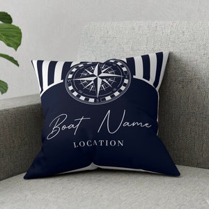 May include: A navy blue throw pillow with white stripes and a compass design. The pillow has the text "Boat Name LOCATION" in white.