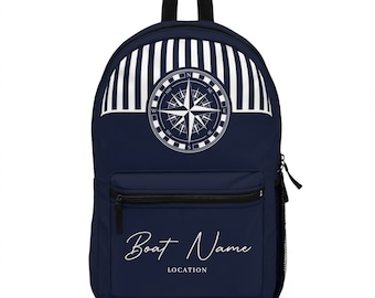 May include: A navy blue backpack with white stripes and a compass design. The backpack has a zippered pocket on the front and the text "Boat Name LOCATION" printed below the compass.