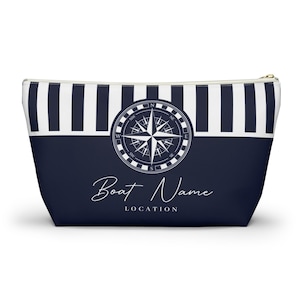 May include: A blue and white striped zippered pouch with a compass design and the text "Boat Name LOCATION".