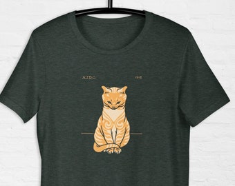 Op de afbeelding: Een donkergroen T-shirt met een vintage illustratie van een oranje tabby-kat. De kat zit met gekruiste poten en heeft een serieuze uitdrukking. De tekst "A.I.D.C." en "1912" staat boven de kat.