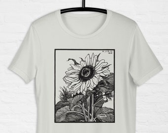 Könnte beinhalten: Ein hellgraues T-Shirt mit einer Schwarzweißillustration einer Sonnenblume. Die Illustration ist in einem schwarzen Rechteck gerahmt mit dem Text "A.J.D.C. 1913" in der oberen rechten Ecke.
