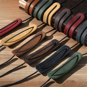 May include: Assortment of colourful leather bookmark straps with elastic bands. The straps are in various colours, including red, yellow, brown, blue, and green.