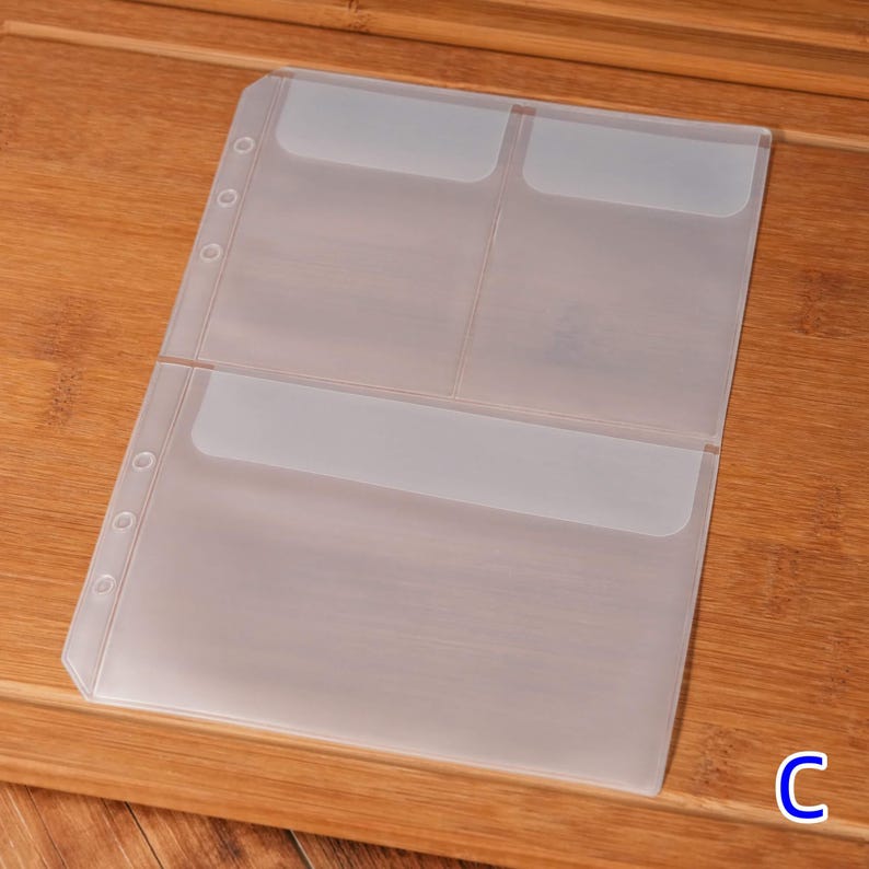 May include: A clear, plastic binder insert with multiple pockets for organizing documents or cards. The insert has pre-punched holes for easy insertion into a binder. The letter "C" is visible in the bottom right corner.