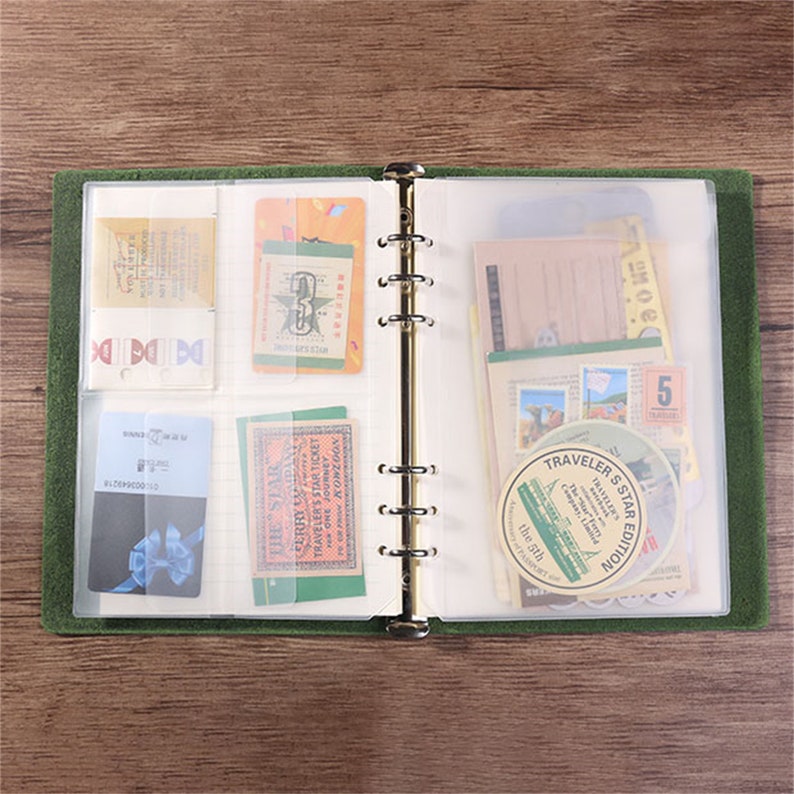 May include: Open green binder with gold rings, filled with various vintage-style ephemera. Includes cards, tickets, and stickers with text like "TRAVELER'S STAR EDITION" and "THE STAR". The binder is open, showcasing the contents.