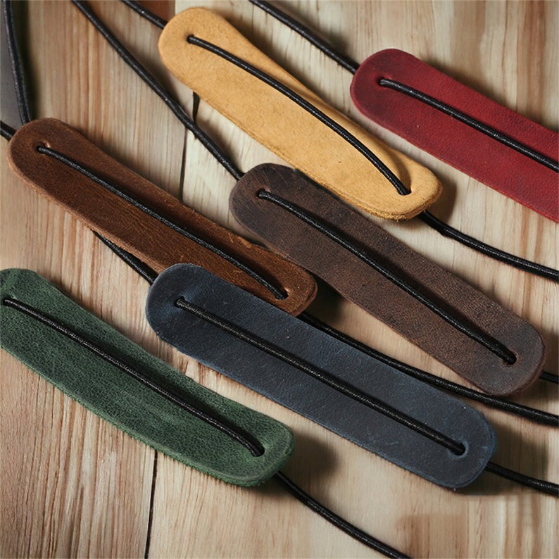 May include: Six leather guitar strap locks in different colors: brown, dark brown, green, blue, yellow, and red. Each lock has a black elastic band running through it.