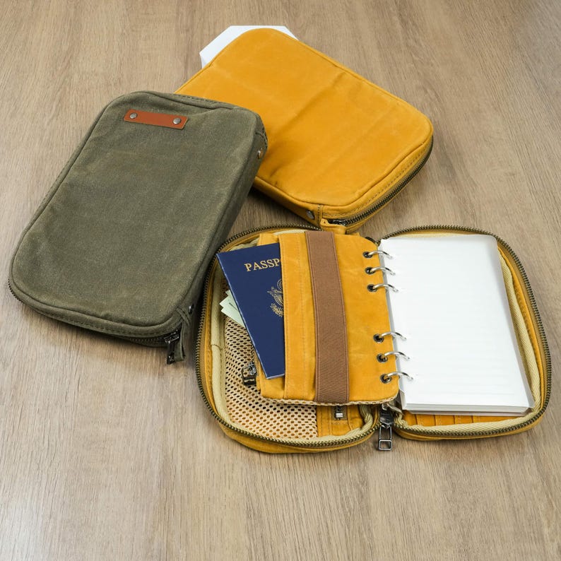 May include: An olive green canvas travel organizer with a brown leather accent and a zippered closure. A mustard yellow organizer is open, revealing a passport, notebook, and mesh pocket. Another mustard yellow organizer is closed.