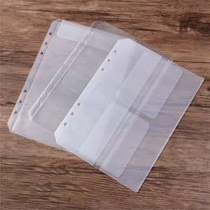 May include: Clear plastic binder sleeves with multiple pockets. The sleeves are designed to hold cards or photos. Each sleeve has pre-punched holes for easy insertion into a binder. The sleeves are arranged on a wooden surface.