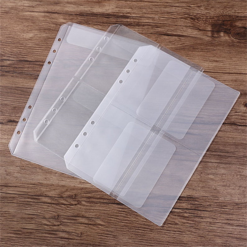May include: Clear plastic binder sleeves with multiple pockets. The sleeves are designed to hold cards or photos. Each sleeve has pre-punched holes for easy insertion into a binder. The sleeves are arranged on a wooden surface.