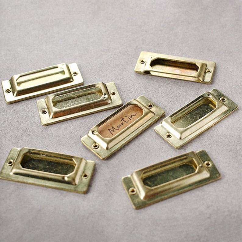 May include: Seven gold-toned metal drawer pulls with a rectangular shape and a recessed center. One pull has the word "Martin" written on it.