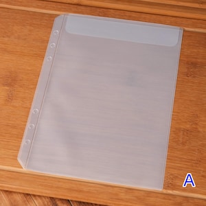 May include: A clear, plastic sheet protector with a reinforced binding edge and pre-punched holes for a three-ring binder. The top edge has a slightly opaque, reinforced section. The letter "A" is visible in the bottom right corner.