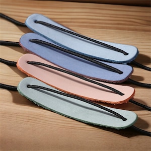 May include: Four leather hair ties in different colors: light blue, blue, pink, and light green. Each tie has a black elastic band.