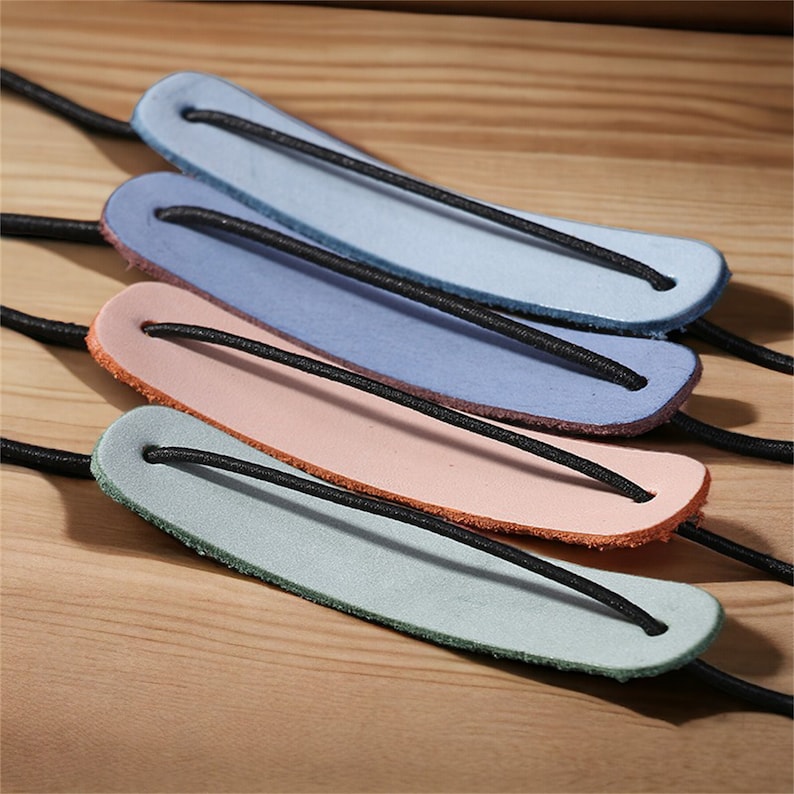 May include: Four leather hair ties in different colors: light blue, blue, pink, and light green. Each tie has a black elastic band.