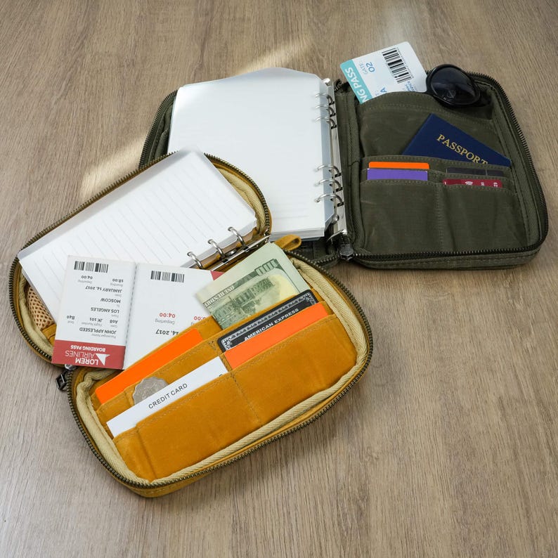 May include: A travel organiser with multiple compartments, including a zippered section with a notebook and another with pockets for a passport, cards, and boarding pass. The organiser is olive green and mustard yellow.