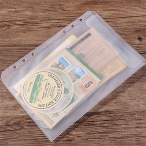 May include: A clear plastic binder sleeve filled with vintage ephemera. The sleeve has three holes for binding and contains postcards, stamps, and circular stickers with text. The stickers read "TRAVELER'S STAR EDITION" and "The Star Ferry Company Limited".