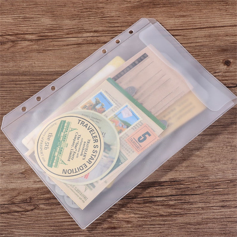 May include: A clear plastic binder sleeve filled with vintage ephemera. The sleeve has three holes for binding and contains postcards, stamps, and circular stickers with text. The stickers read "TRAVELER'S STAR EDITION" and "The Star Ferry Company Limited".
