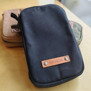 May include: A black canvas zippered pouch with a leather tag that reads "SOLOKING". A brown canvas pouch and a green canvas pouch are visible in the background. The pouches have a rectangular shape.