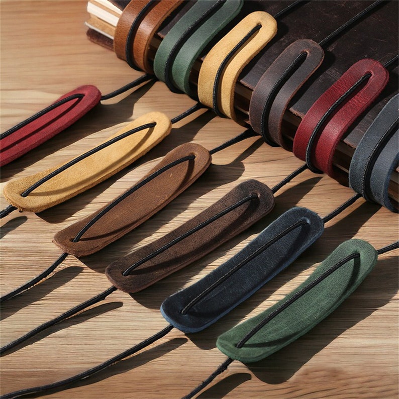 May include: Assortment of colorful leather bookmark straps with elastic bands. The straps are in various colors, including red, yellow, brown, blue, and green.