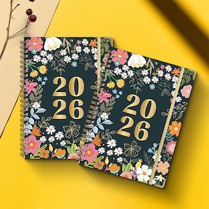 May include: Two spiral-bound 2026 planners with floral designs. The covers are dark teal with gold accents and the numbers "20 26" in gold. The floral pattern includes pink, orange, white, and yellow flowers with green leaves.