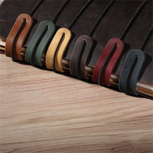 May include: A leather-bound journal with eight colorful leather bookmarks. The bookmarks are in shades of brown, red, green, yellow, and black.