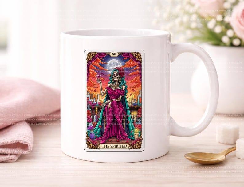 Puede incluir: Una taza de cer&aacute;mica blanca con una colorida ilustraci&oacute;n de carta de tarot titulada THE SPIRITED. La imagen muestra una figura esquel&eacute;tica con cabello verde azulado en un vestido magenta, sosteniendo una copa frente a un cielo al atardecer.