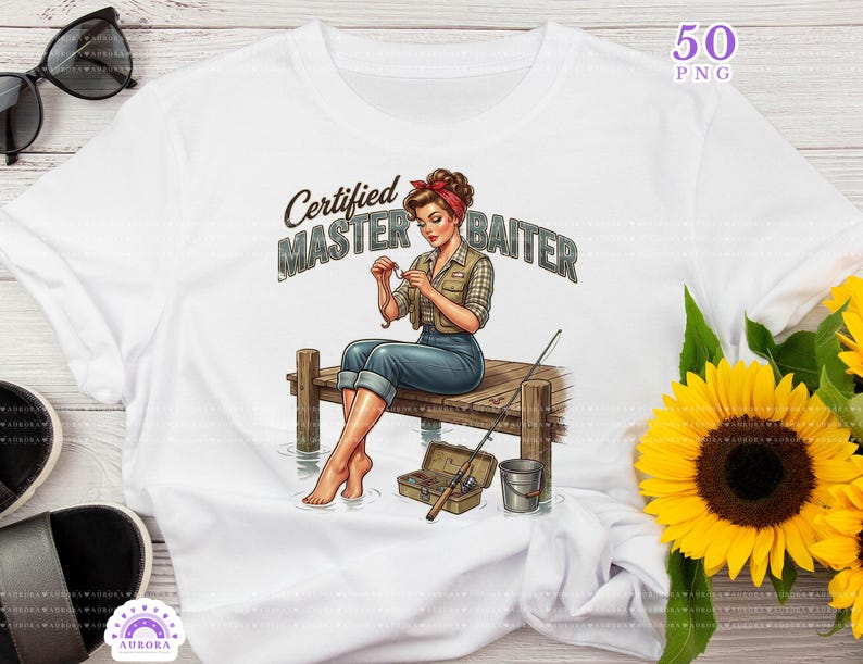 May include: White t-shirt featuring a graphic of a woman fishing, seated on a dock. The text "Certified Master Baiter" is above the woman. The image includes a fishing rod, tackle box, and a bucket. A pair of sunglasses and a sunflower are also visible.