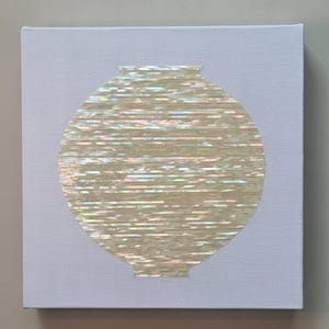 Peut inclure: Une toile carrée blanche présentant une silhouette de vase circulaire centrée, composée de fragments horizontaux de nacre irisée. Les morceaux de coquillage affichent une finition nacrée chatoyante et multicolore sur le fond blanc uni.