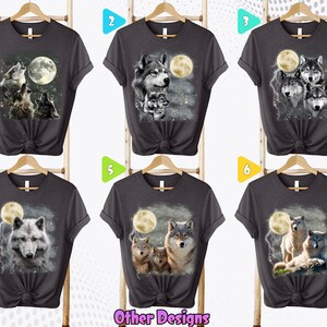 K&ouml;nnte beinhalten: Sechs verschiedene graue T-Shirts mit Wolf- und Mondmotiven. Die Shirts werden auf Kleiderb&uuml;geln vor einem wei&szlig;en Hintergrund pr&auml;sentiert. Die Zahlen 1 bis 6 werden in bunten Kreisen &uuml;ber jedem Shirt angezeigt.