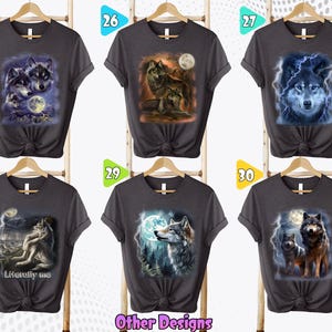 K&ouml;nnte beinhalten: Sechs graue T-Shirts mit verschiedenen Wolf-Designs. Die Designs beinhalten einen Wolf, der zum Mond heult, einen Wolf mit Blitz und einen Wolf mit einem blauen Leuchten. Die Shirts h&auml;ngen alle an Kleiderb&uuml;geln und haben einen wei&szlig;en Hintergrund.