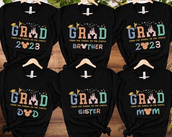 May include: Six black t-shirts with a colourful graphic of a castle, Mickey Mouse ears, and the text "GRAD FROM THE TASSEL TO THE CASTLE" with different text below the graphic. The text below the graphic on the shirts reads "2023", "BROTHER", "MOM", "DAD", "SISTER", and "2023".