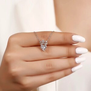 May include: A silver necklace with a heart-shaped pendant topped with a crown, both adorned with clear cubic zirconia stones.