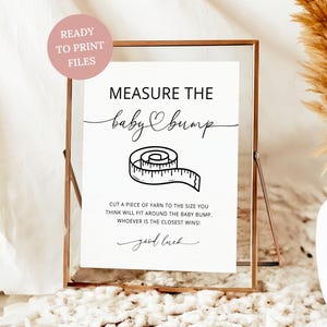 May include: A framed white sign with the text "MEASURE THE baby bump" and a measuring tape illustration. The sign includes the text "CUT A PIECE OF YARN TO THE SIZE YOU THINK WILL FIT AROUND THE BABY BUMP. WHOEVER IS THE CLOSEST WINS! good luck."