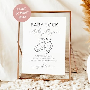 Op de afbeelding: Een ingelijst bord met de tekst "BABY SOCK matching Game" en een illustratie van twee babysokken. Het bord bevat de tekst "MATCH THE BABY SOCKS BEFORE THE TIMER RUNS OUT! WHOEVER MATCHES THE MOST WINS!" en "good luck."