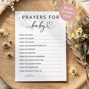 Puede incluir: Una taza de cerámica blanca con un asa negra y el texto "But First, Coffee" en negrita negra. La taza se encuentra sobre un fondo borroso, sugiriendo un ambiente acogedor.