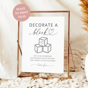 May include: A framed sign with the text "DECORATE A block" and an illustration of three stacked blocks. The sign includes the text "HELP US BUILD MEMORIES AND DECORATE A BLOCK FOR BABY. DON'T FORGET TO SIGN YOUR NAME!" and "READY TO PRINT FILES".