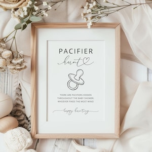 K&ouml;nnte beinhalten: Ein rechteckiger Holzrahmen mit einem wei&szlig;en Schild mit schwarzem Text, der PACIFIER hunt lautet, einer Strichzeichnung eines Schnullers und der Anweisung: THERE ARE PACIFIERS HIDDEN THROUGHOUT THE BABY SHOWER. WHOEVER FINDS THE MOST WINS! gefolgt von happy hunting.