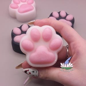 May include: Close-up of paw-shaped soaps in white and black with pink paw prints. One soap is held in a hand. The soaps are arranged on a light pink surface. The Lilipond logo is visible.