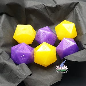 Può includere: Sei dadi poliedrici gialli e viola, disposti su carta nera. I dadi sono numerati e hanno una finitura lucida, adatti per i giochi da tavolo. I dadi sono un mix di forme D20 e D10.