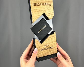 May include: A wooden award plaque with a black and clear acrylic insert. The plaque has the text "IELCA Holding" and "2024 APDovanoJIMAI" engraved on it. The acrylic insert has the text "ATVERTA SIELA" engraved on it.